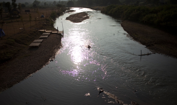 Man fishing and bathing in the river below the memorial bridge in Pai